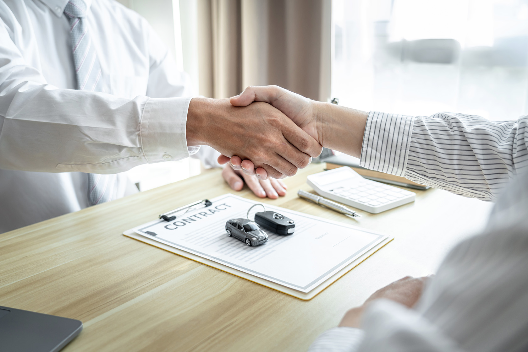 A custoemr and salesman shake hands over a car insurance form